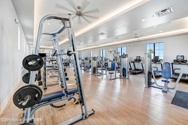 workout area with a ceiling fan, visible vents, baseboards, and wood finished floors