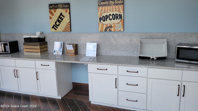 kitchen featuring white cabinets, built in study area, stainless steel microwave, wood finish floors, and backsplash