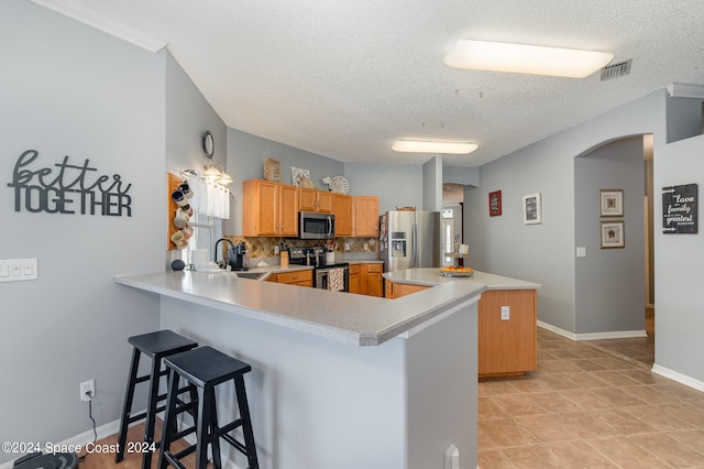 kitchen with a textured ceiling, kitchen peninsula, decorative backsplash, stainless steel appliances, and a kitchen breakfast bar