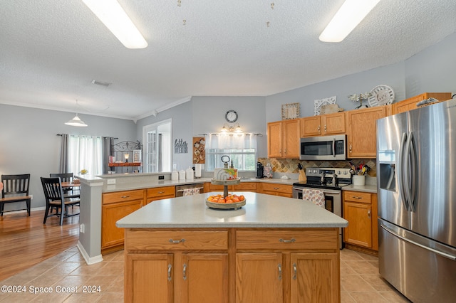 kitchen with appliances with stainless steel finishes, ornamental molding, kitchen peninsula, and a kitchen island