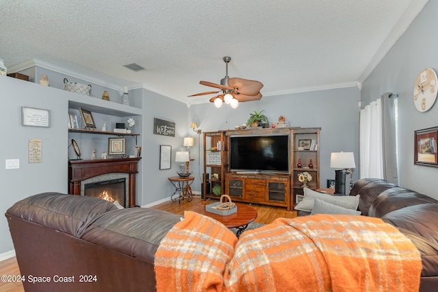 living room featuring ornamental molding, light hardwood / wood-style floors, ceiling fan, and a textured ceiling