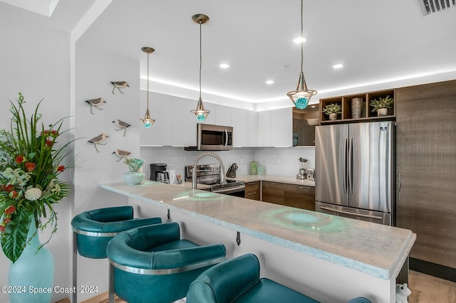 kitchen with light stone countertops, appliances with stainless steel finishes, tasteful backsplash, kitchen peninsula, and white cabinetry