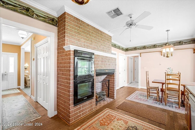 interior space with a fireplace, light hardwood / wood-style flooring, black double oven, crown molding, and ceiling fan