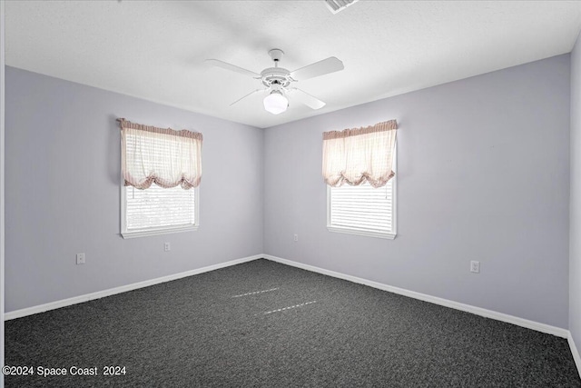 empty room with ceiling fan and dark colored carpet