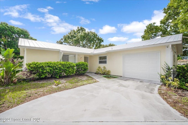 ranch-style home featuring stucco siding, an attached garage, concrete driveway, and metal roof