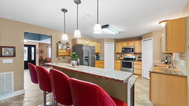 kitchen featuring backsplash, decorative light fixtures, stainless steel appliances, sink, and a breakfast bar