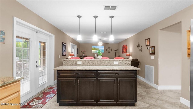 kitchen featuring pendant lighting, dark brown cabinets, and light stone countertops