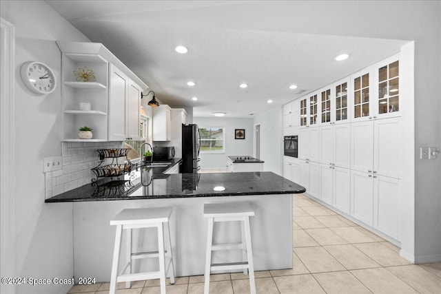 kitchen featuring dark stone counters, kitchen peninsula, stainless steel refrigerator, and white cabinets