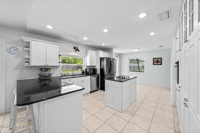 kitchen featuring dark stone counters, stainless steel appliances, kitchen peninsula, sink, and white cabinets