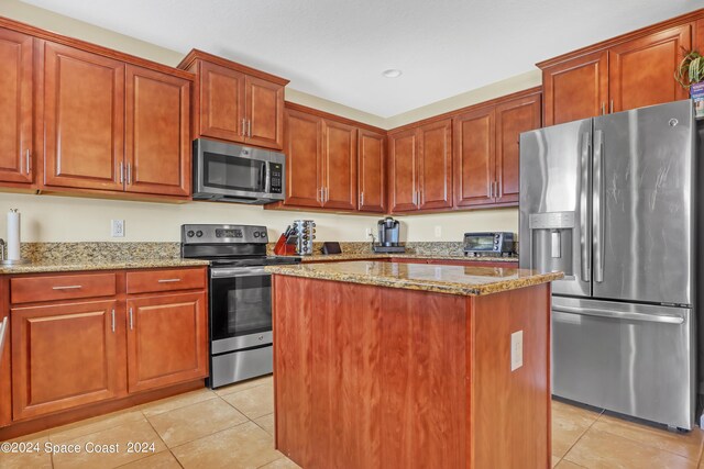 kitchen with appliances with stainless steel finishes, light stone counters, a kitchen island, and light tile patterned flooring