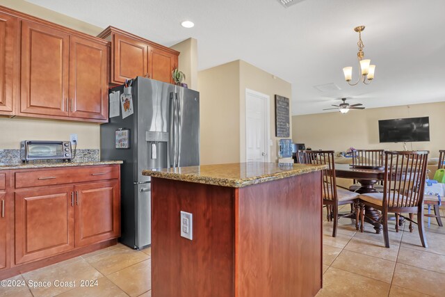 kitchen featuring stainless steel fridge with ice dispenser, ceiling fan with notable chandelier, a center island, and light stone countertops