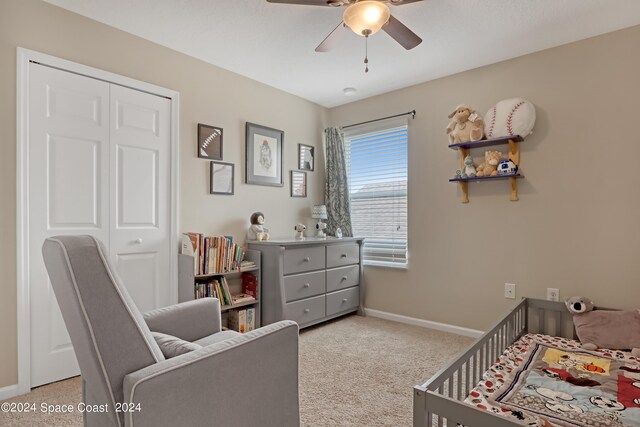 carpeted bedroom featuring a closet, ceiling fan, and a nursery area