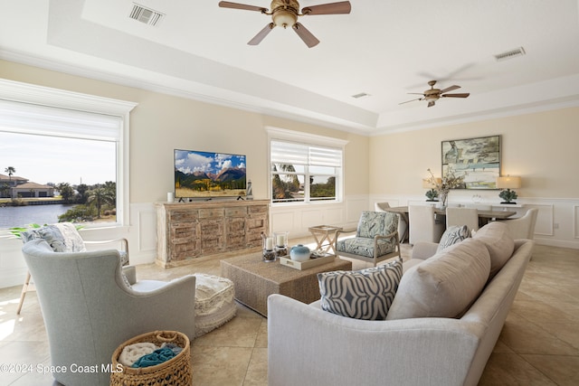 tiled living room with a water view, ceiling fan, and a raised ceiling