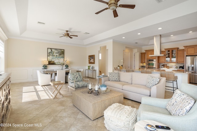 tiled living room with crown molding, ceiling fan, and a raised ceiling