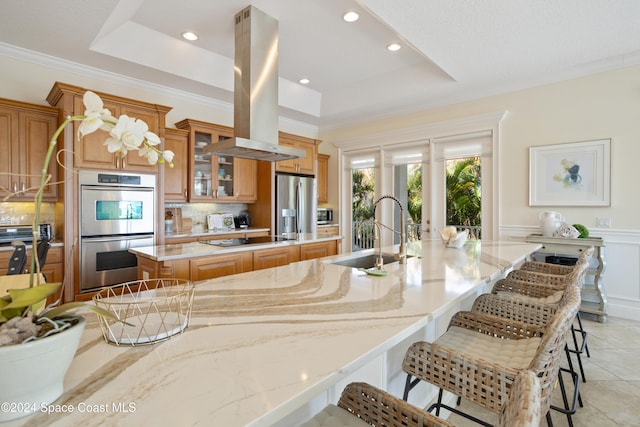 kitchen featuring island range hood, stainless steel appliances, backsplash, a large island with sink, and a breakfast bar