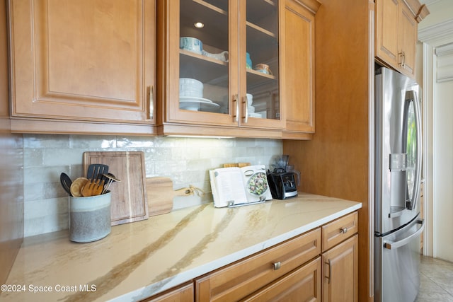 kitchen with light stone countertops, decorative backsplash, and stainless steel fridge