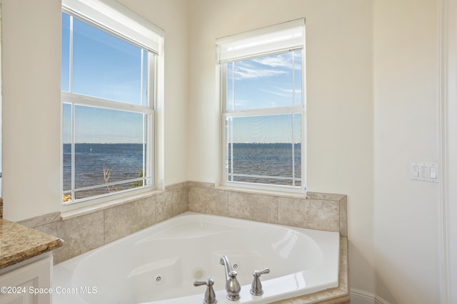 bathroom with a water view, a healthy amount of sunlight, vanity, and tiled tub