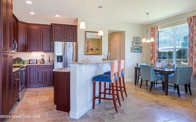 kitchen featuring light stone counters, stainless steel appliances, a notable chandelier, a breakfast bar area, and pendant lighting