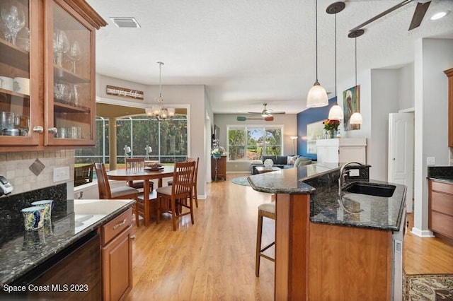 kitchen featuring backsplash, ceiling fan with notable chandelier, brown cabinets, light wood-style floors, and a sink