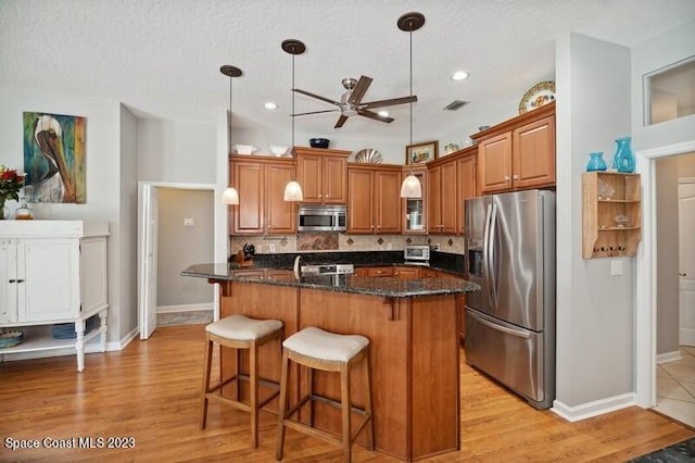 kitchen featuring a textured ceiling, decorative light fixtures, light hardwood / wood-style flooring, stainless steel appliances, and ceiling fan