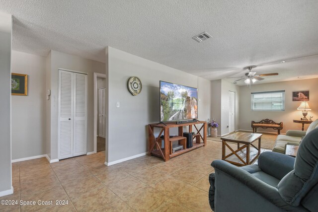 living room with a textured ceiling, ceiling fan, and light tile patterned floors