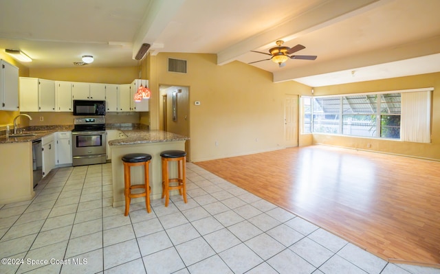 kitchen with vaulted ceiling with beams, dark stone counters, black appliances, a breakfast bar, and light wood-type flooring