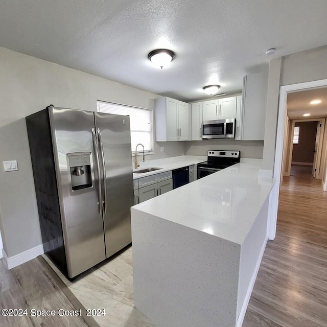 kitchen with a textured ceiling, stainless steel appliances, sink, kitchen peninsula, and light wood-type flooring