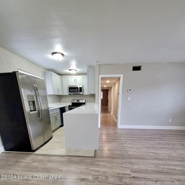 kitchen featuring light wood-type flooring, appliances with stainless steel finishes, white cabinetry, and a textured ceiling