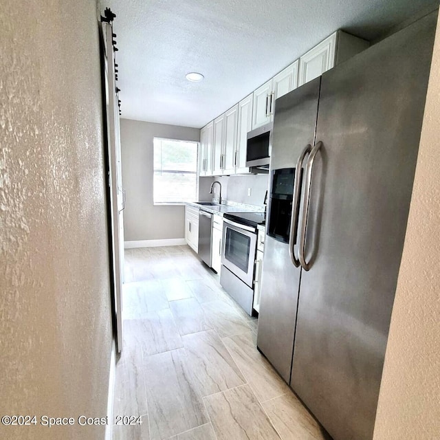 kitchen with a textured ceiling, stainless steel appliances, sink, and white cabinetry