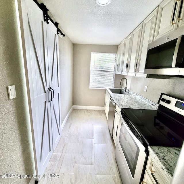 kitchen with a barn door, light stone countertops, stainless steel appliances, and sink