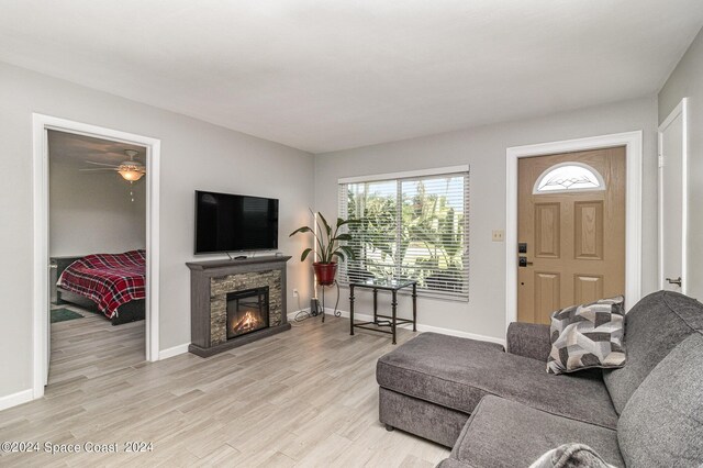 living room featuring light hardwood / wood-style flooring, ceiling fan, and a stone fireplace