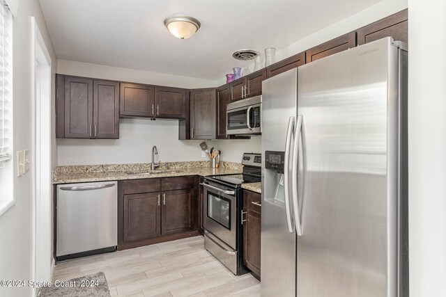 kitchen featuring appliances with stainless steel finishes, sink, light stone countertops, dark brown cabinets, and light hardwood / wood-style flooring