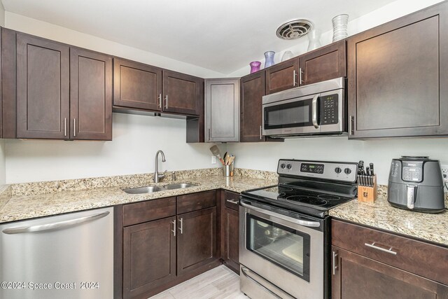 kitchen featuring light stone counters, stainless steel appliances, dark brown cabinets, and sink