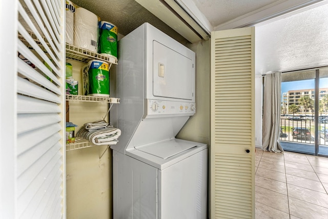 clothes washing area with stacked washer and clothes dryer, a textured ceiling, and light tile patterned flooring