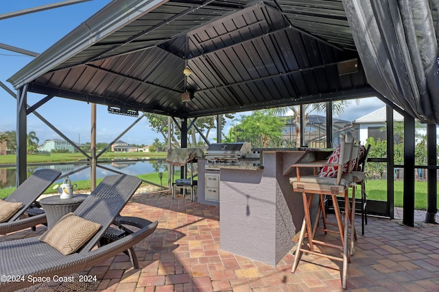 view of patio / terrace featuring an outdoor kitchen, a lanai, grilling area, a water view, and a bar