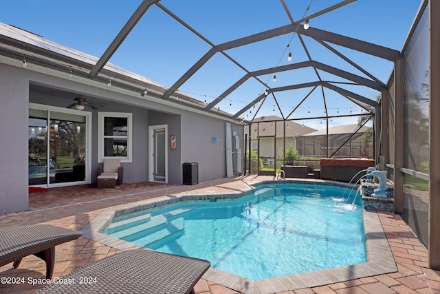 view of pool with glass enclosure, pool water feature, ceiling fan, a patio, and a hot tub