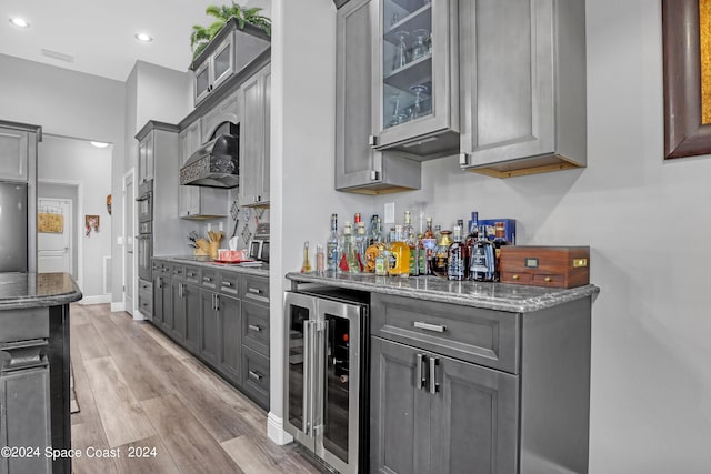 kitchen with light hardwood / wood-style floors, wall chimney exhaust hood, beverage cooler, stone countertops, and gray cabinets