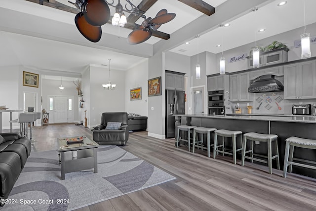 living room featuring a towering ceiling, light hardwood / wood-style flooring, beamed ceiling, and ceiling fan with notable chandelier