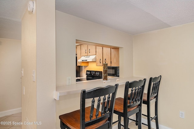 kitchen featuring a textured ceiling, black appliances, built in desk, light brown cabinetry, and light tile patterned flooring