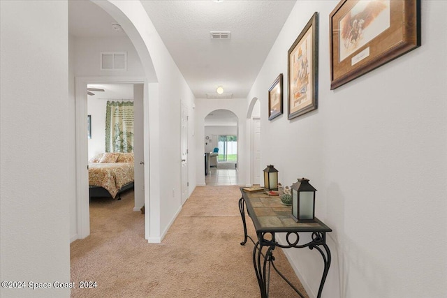 hallway with a textured ceiling and light colored carpet