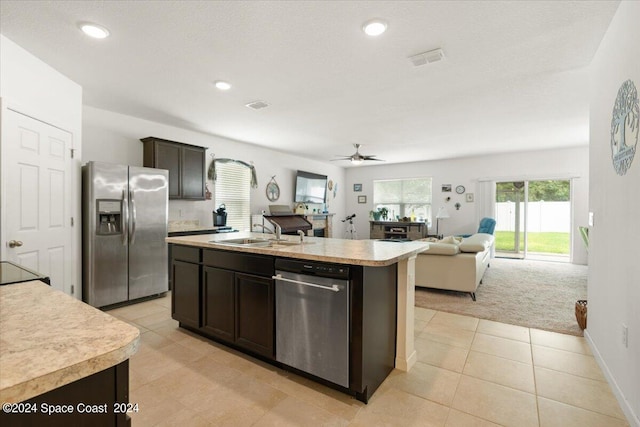 kitchen with light carpet, appliances with stainless steel finishes, an island with sink, sink, and ceiling fan