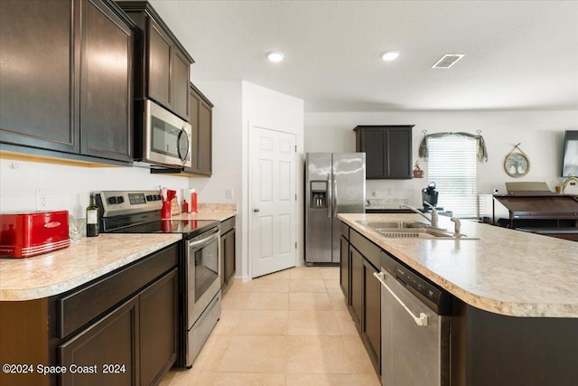 kitchen with a textured ceiling, light tile patterned floors, appliances with stainless steel finishes, a kitchen island with sink, and sink