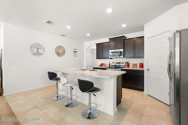 kitchen with dark brown cabinets, appliances with stainless steel finishes, an island with sink, a kitchen bar, and sink