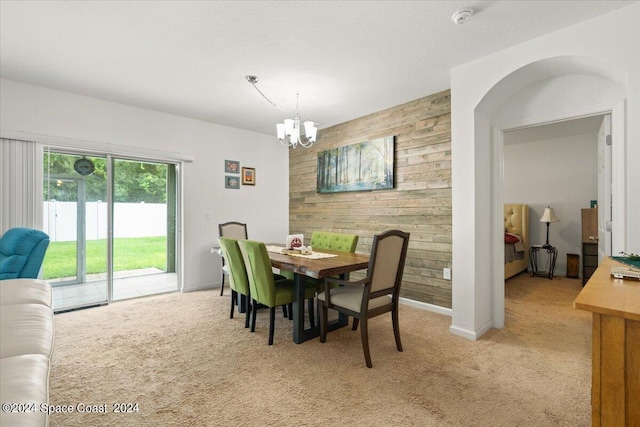 dining room featuring light carpet, a textured ceiling, a chandelier, and wooden walls