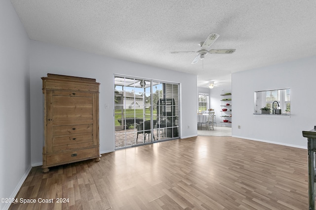 interior space with a textured ceiling, a sink, wood finished floors, a ceiling fan, and baseboards