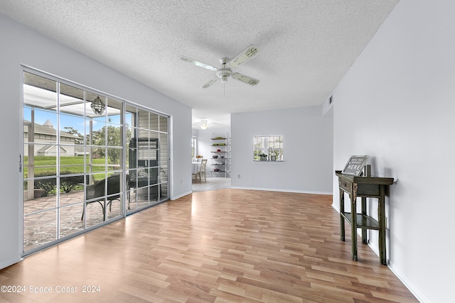 unfurnished living room with a wealth of natural light, light hardwood / wood-style floors, ceiling fan, and a textured ceiling