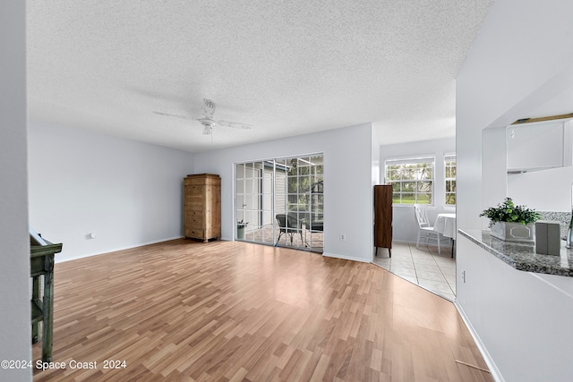 unfurnished living room with a textured ceiling, light hardwood / wood-style floors, and ceiling fan