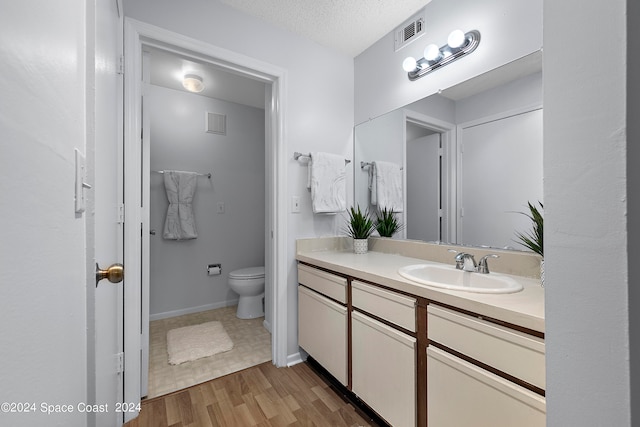 bathroom with a textured ceiling, wood-type flooring, vanity, and toilet