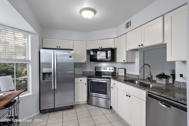 kitchen featuring appliances with stainless steel finishes, light tile patterned flooring, white cabinetry, dark stone counters, and sink