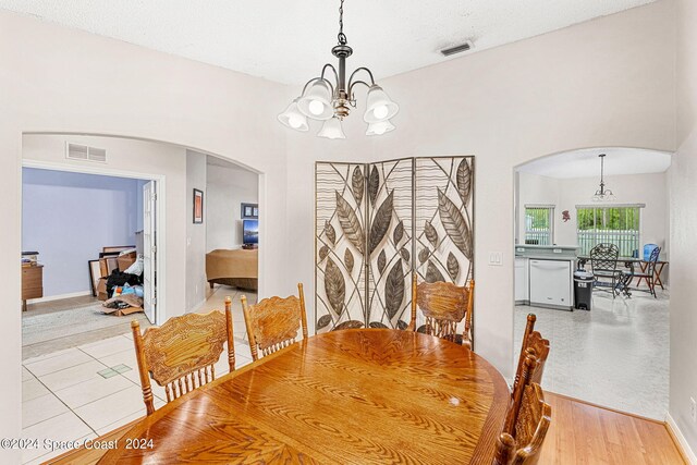 dining room with light wood-type flooring, a textured ceiling, and a notable chandelier